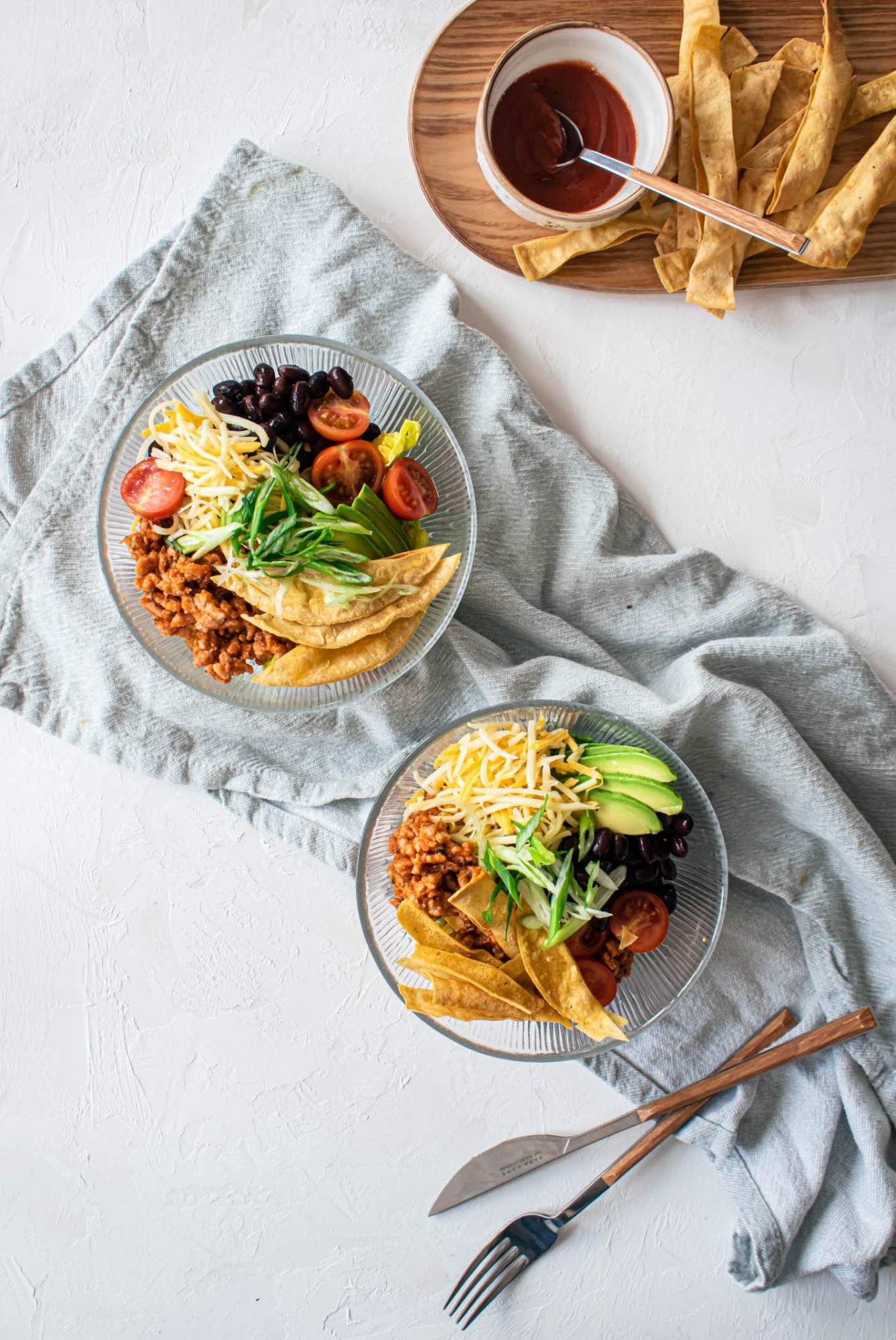 Ground turkey taco salad in two bowls with turkey taco meat, shredded cheese, avocado, black beans, and tomatoes.