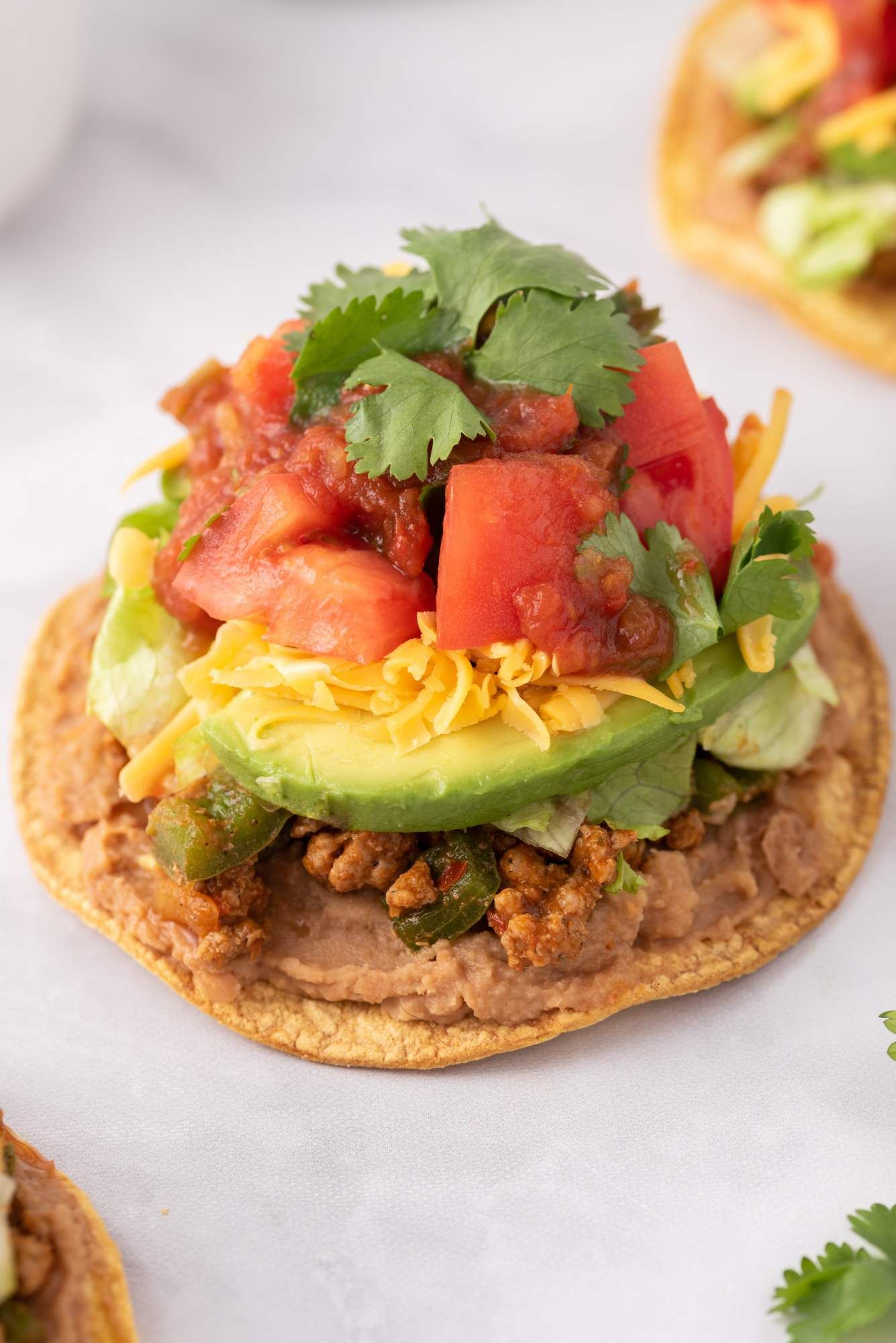 Tostada with ground turkey, refried beans, salsa, avocado, lettuce, and shredded cheese.