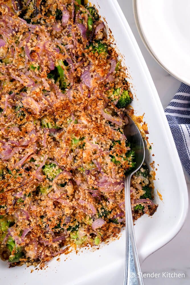 Broccoli casserole with crispy red onion, breadcrumbs, and mushrooms in a ceramic dish.