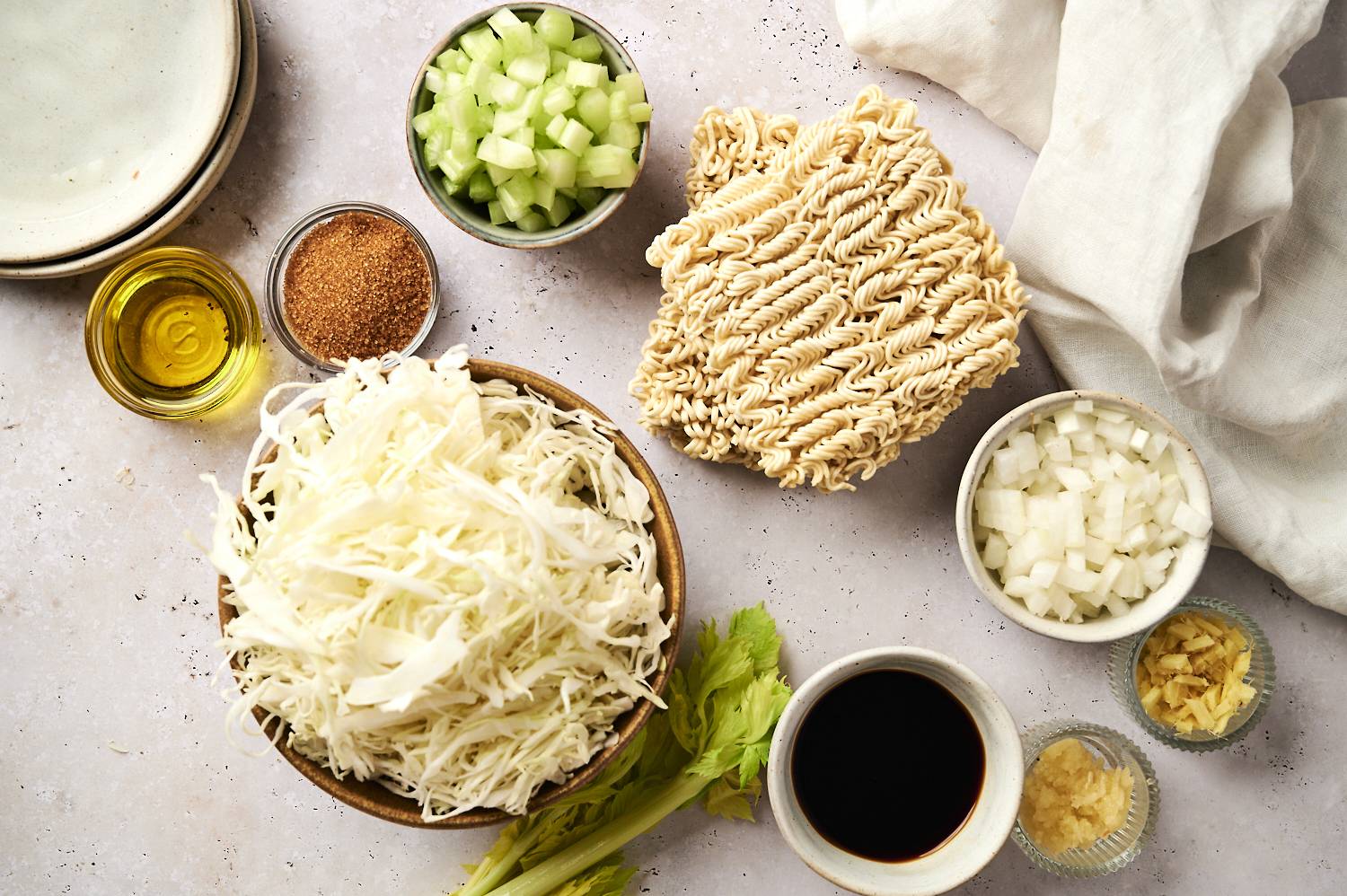 Ingredients for healthy chow mein including yaki soba noodles, cabbage, celery, spices, onion, garlic, ginger, and oil.