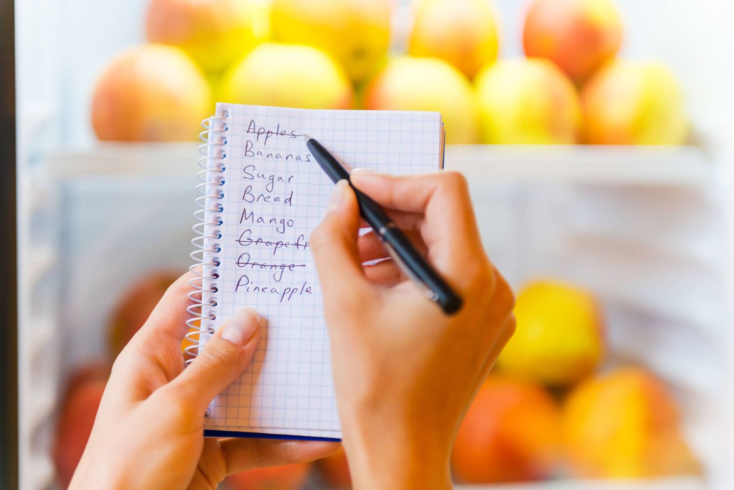 Shopping list for a healthy meal plan with fruit in the background.