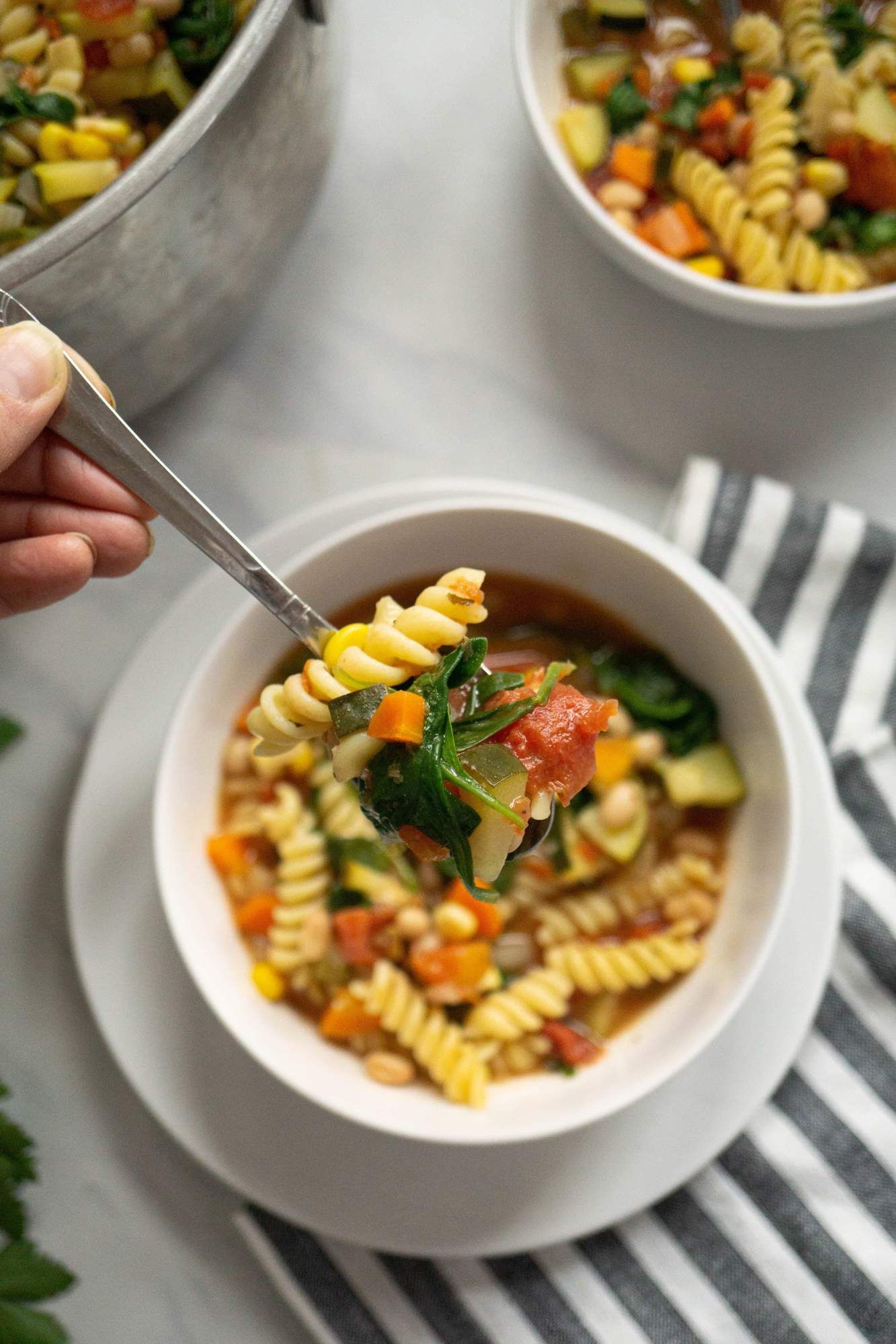 Minestrone soup with vegetables, pasta, and white beans on a spoon.