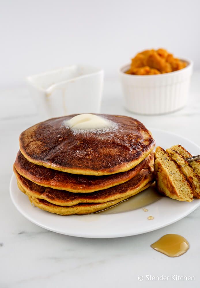 Healthy pumpkin pie recipe on a plate with maple syrup and pumpkin in the background.