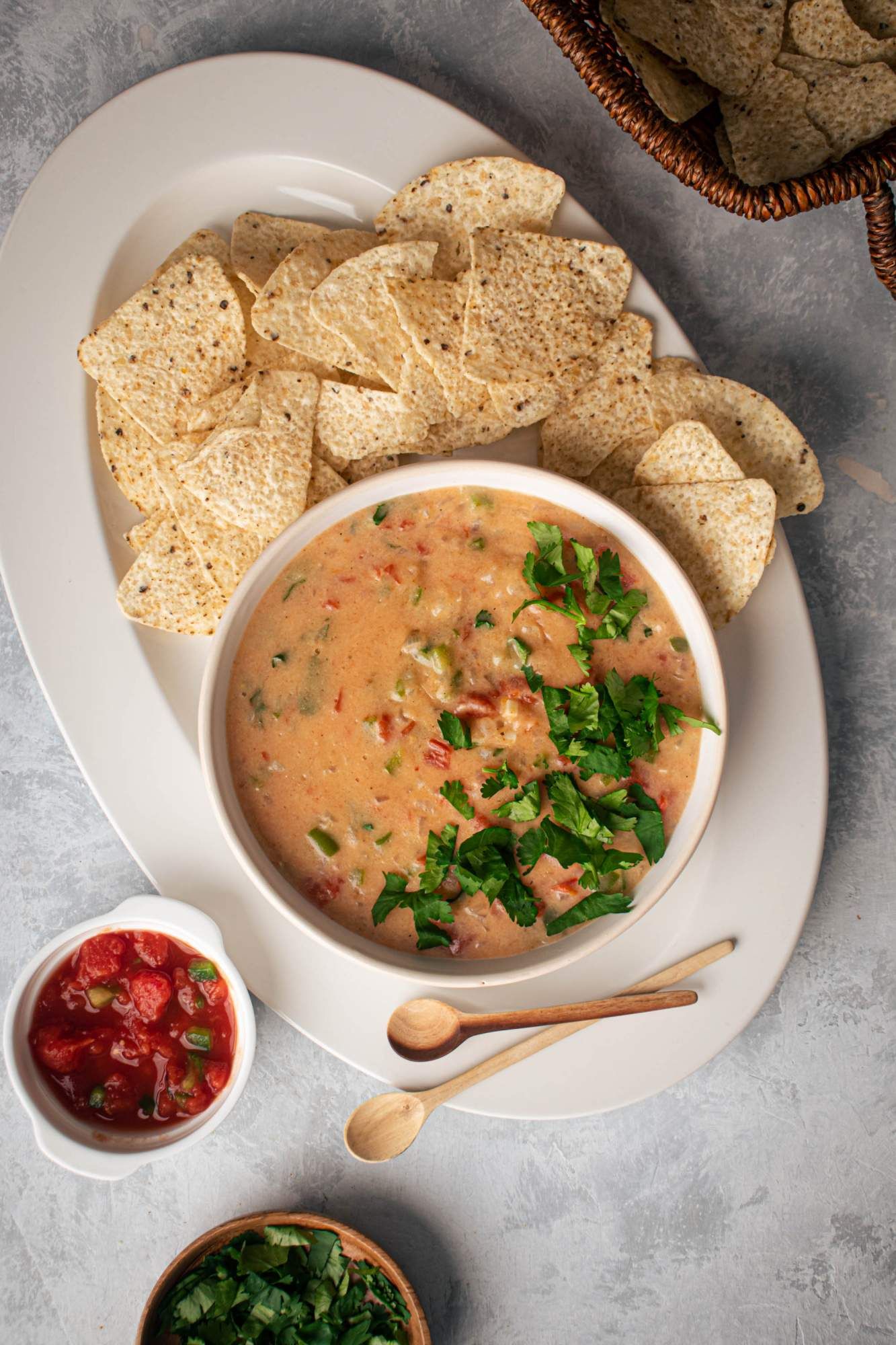 Queso dip with melted cheddar, cheese, diced tomatoes, green chilies, and cilantro on a plate with tortilla chips and cilantro.