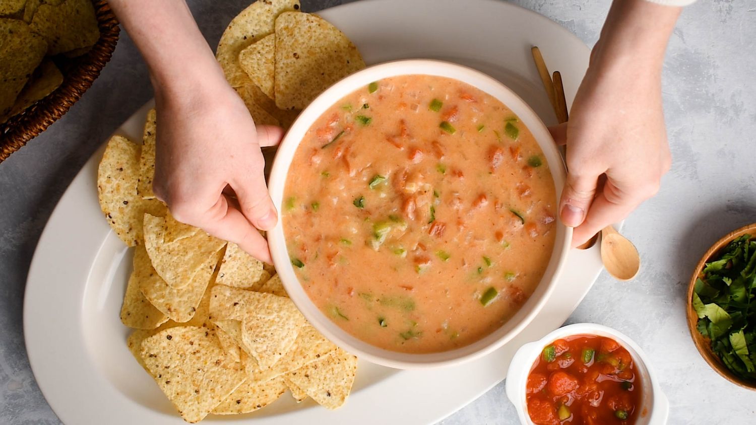 Lightened up cheddar queso dip in a bowl with two hands holding it and tortilla chips.