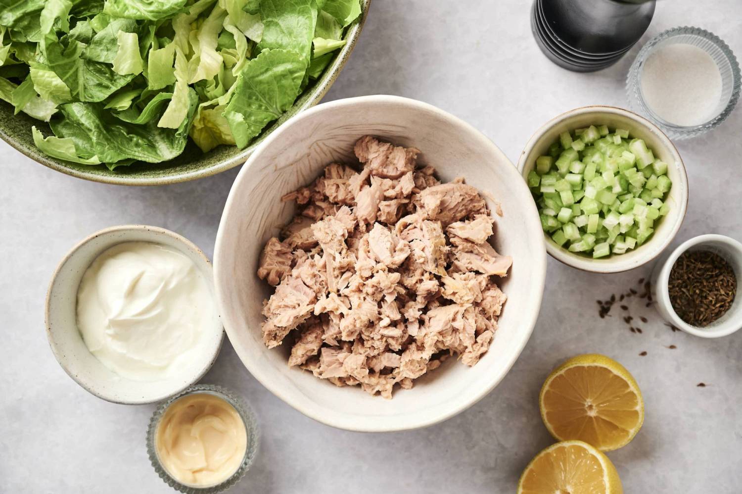 Ingredients for healthy tuna salad including canned tuna, mayonnaise, Greek yogurt, celery, and lemon juice.