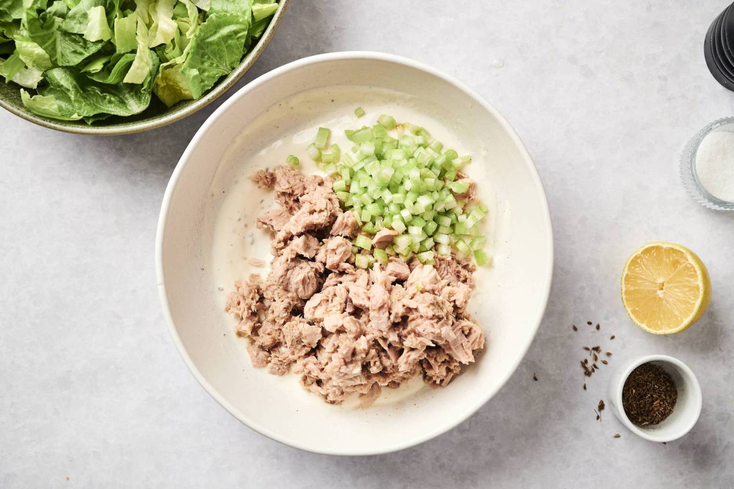 Canned tuna in a bowl with diced celery, mayo, lemon juice, black pepper, salt, and celery seed.