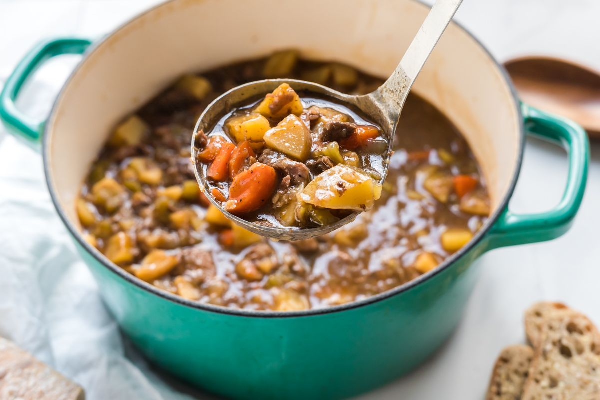 A ladle full of beef stew with fork tender beef, potatoes, carrots, onions, and celery.