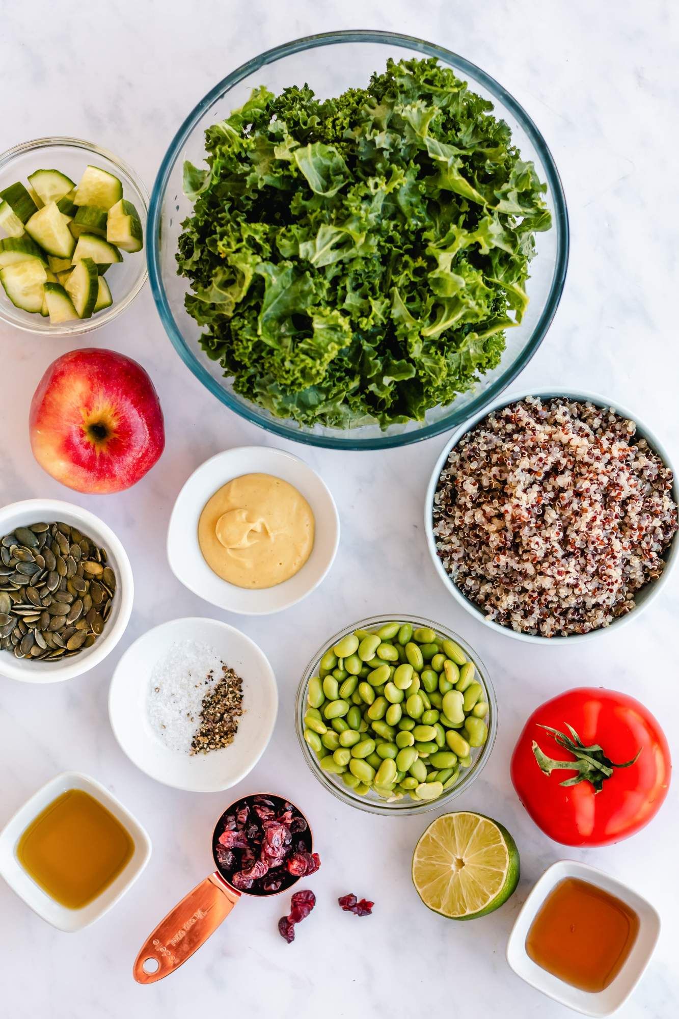 Ingredients for kale quinoa salad with cooked quinoa, massaged kale, apples, edamame, honey lime dressing, and more.