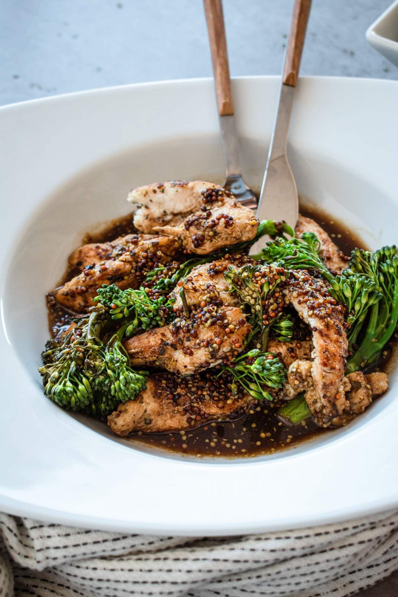 Chicken in honey mustard sauce with broccolini in a bowl with a fork and knife.