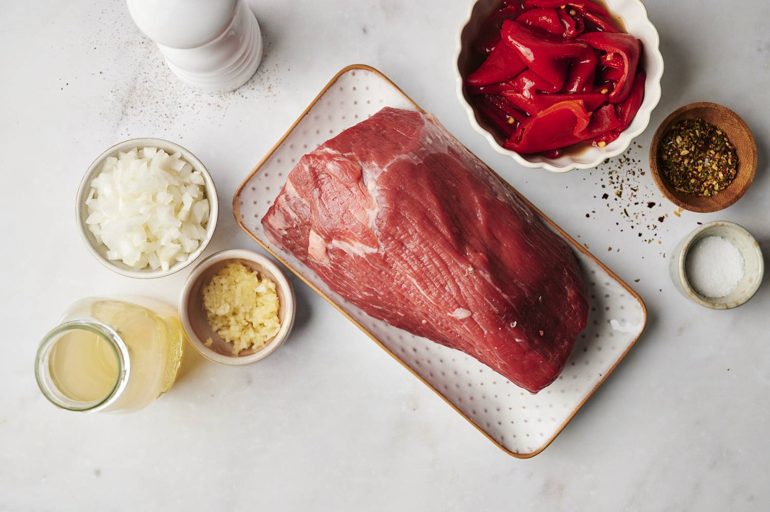 Ingredients for drip beef laid out, including the roast, beef broth, pepperonici peppers and seasonings 