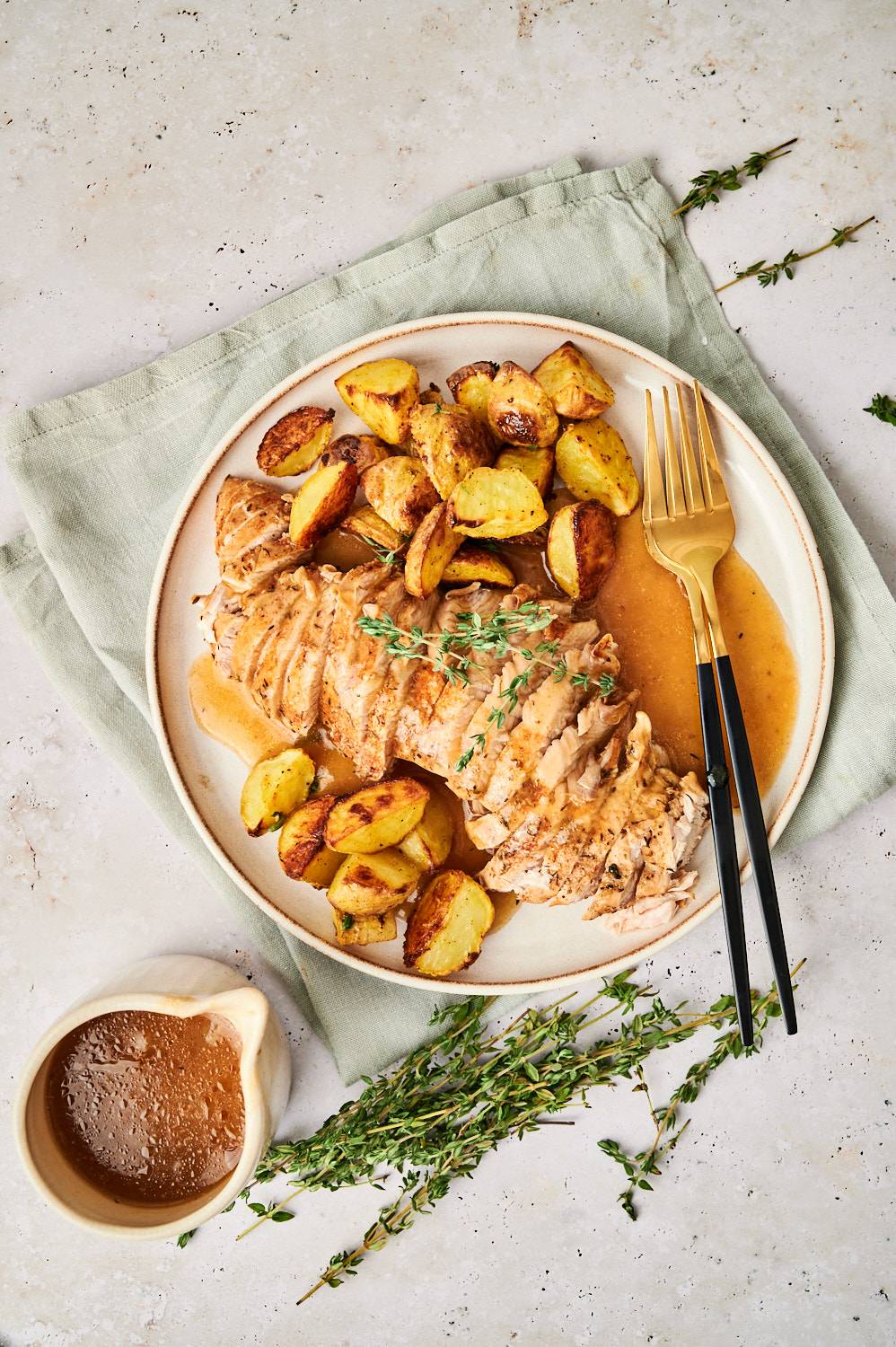 Sliced instant pot turkey tenderloin on a plate with roasted potatoes and herbs.