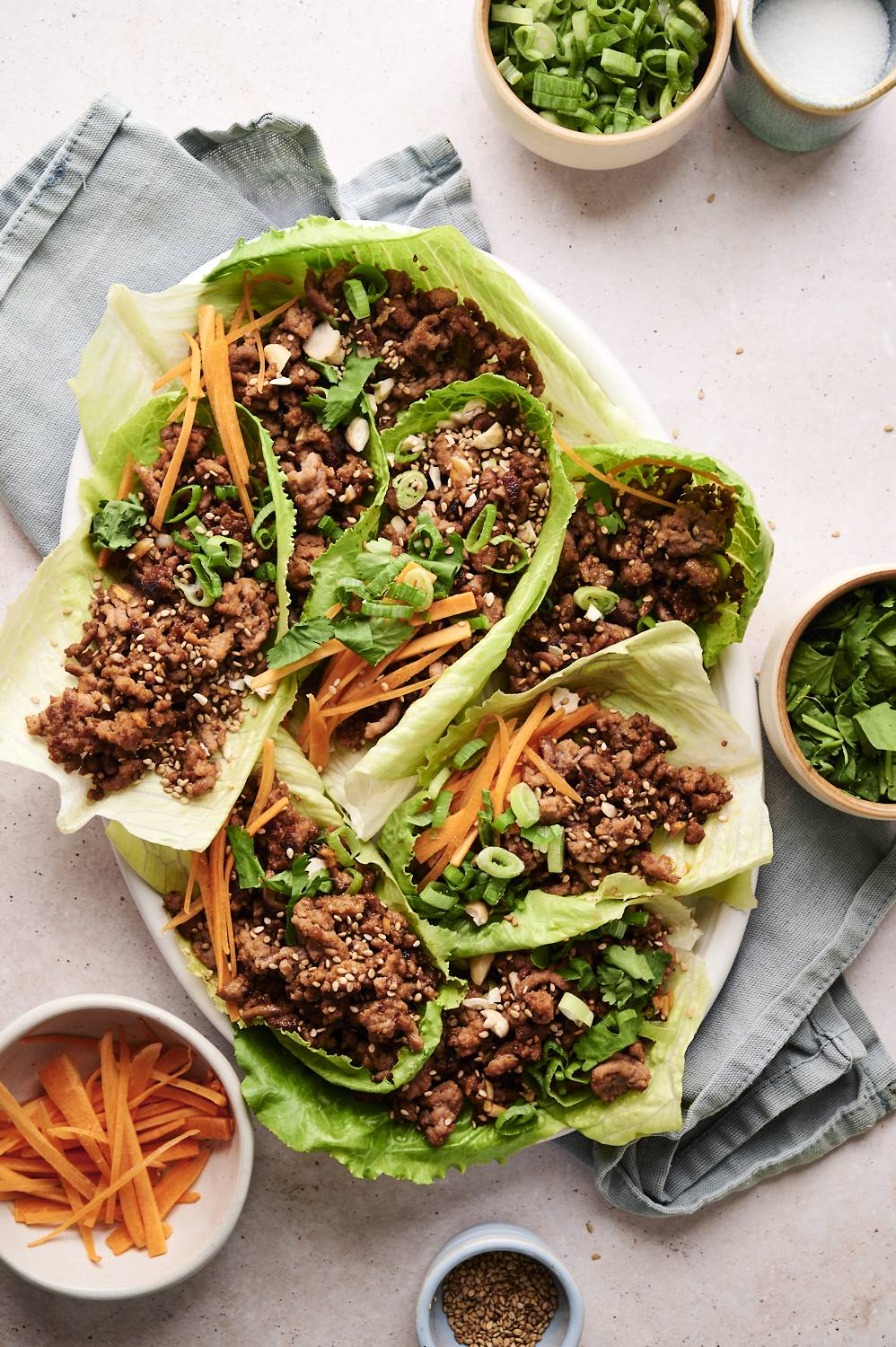 A bowl of Korean beef lettuce wraps, with a pair of chopsticks and a side of shredded carrots.