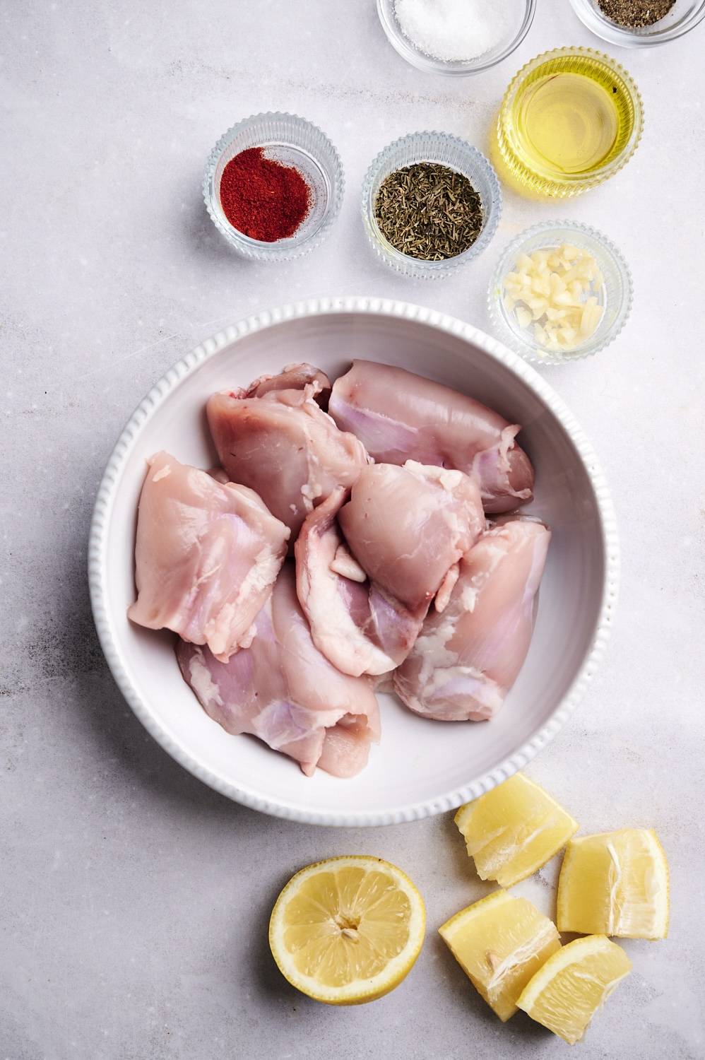 Ingredients for paprika chicken thighs including chicken thighs, lemon, garlic, paprika, thyme, salt, pepper, and olive oil.