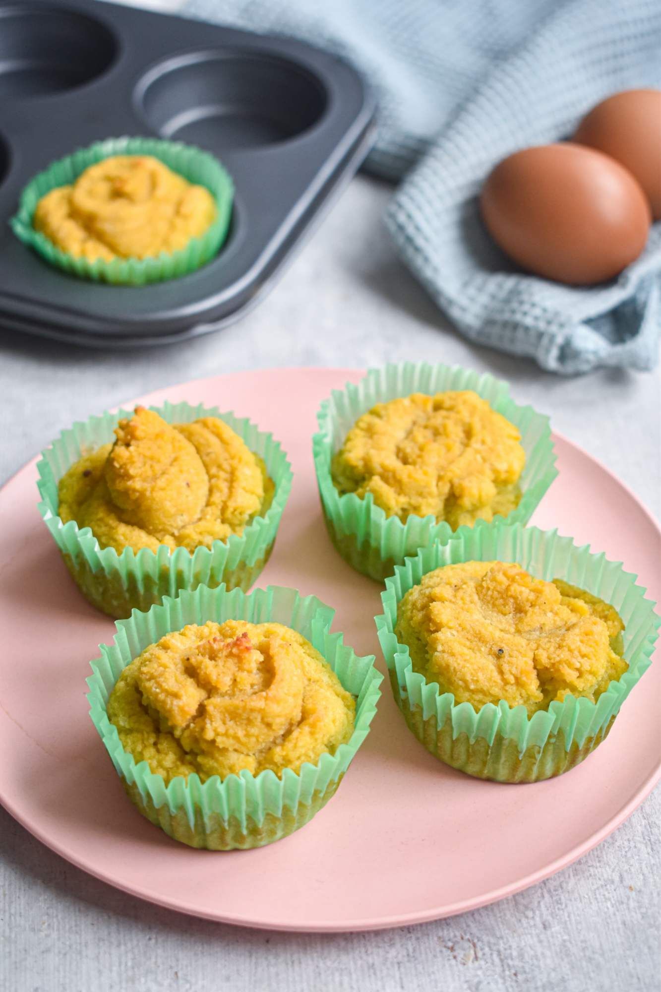 Keto coconut muffins on a pink plate with a muffin tin in the background.