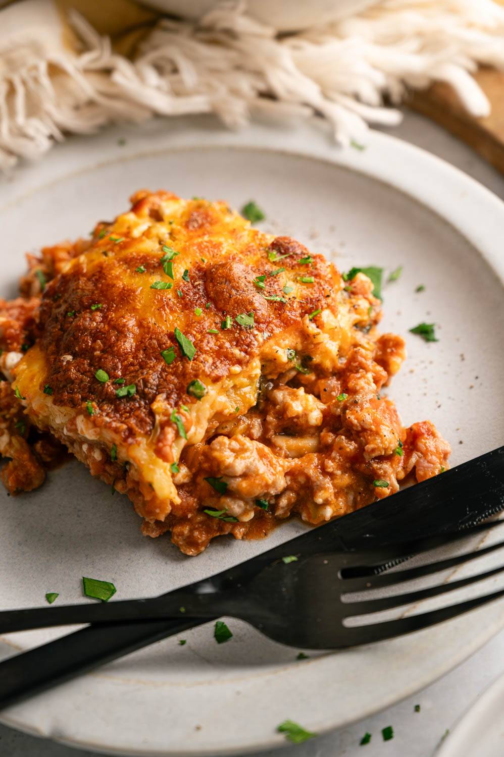 A savory slice of lasagna on a gray plate, topped with melted cheese and sprinkled with parsley.