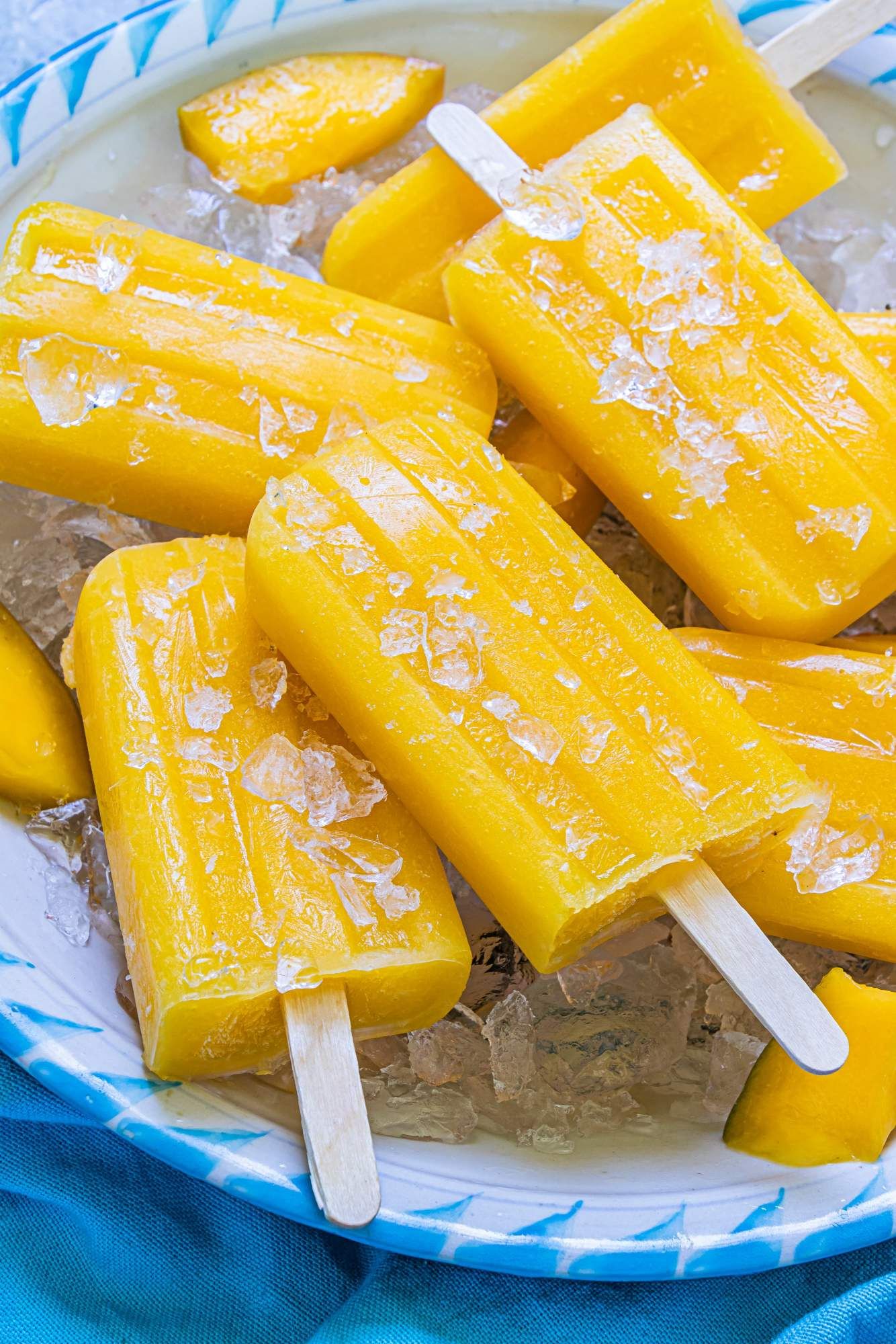 Homemade mango popsicles with fresh mango on a blue and white plate.