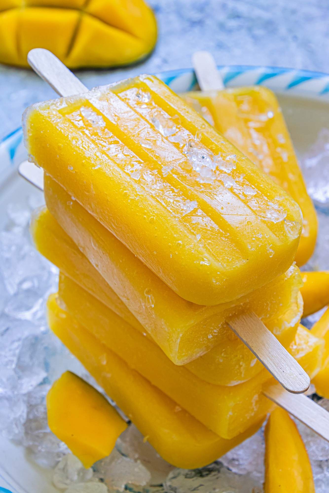 Popsicles made with mango, honey, and lime stacked on a plate with ice.