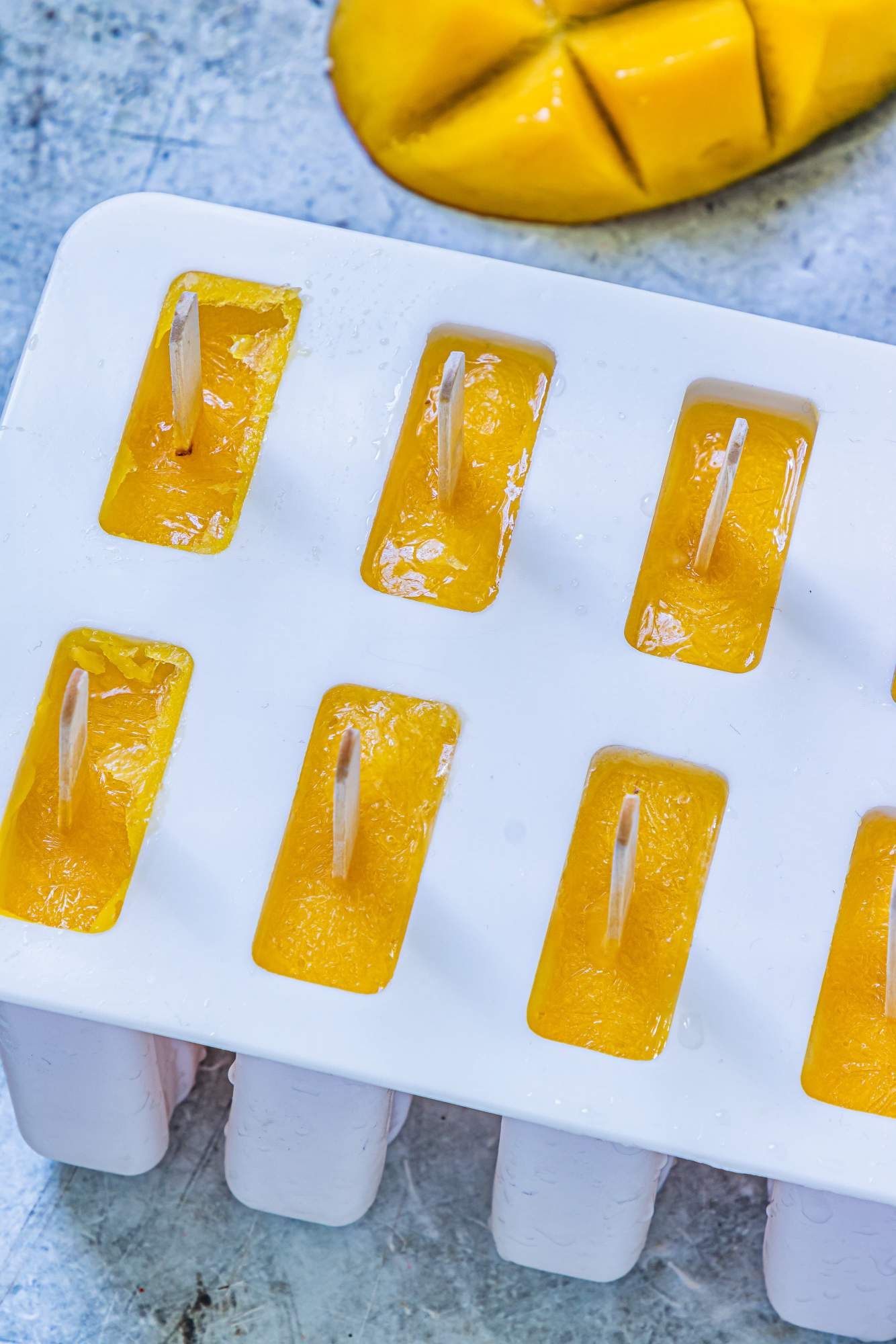 Popsicle molds filled with mango puree ready to be frozen into popsicles.