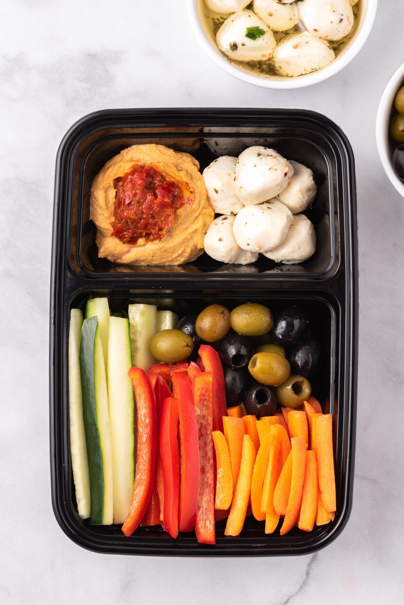 Bistro box with hummus, olives, mozzarella cheese, cucumbers, bell peppers, and carrots.
