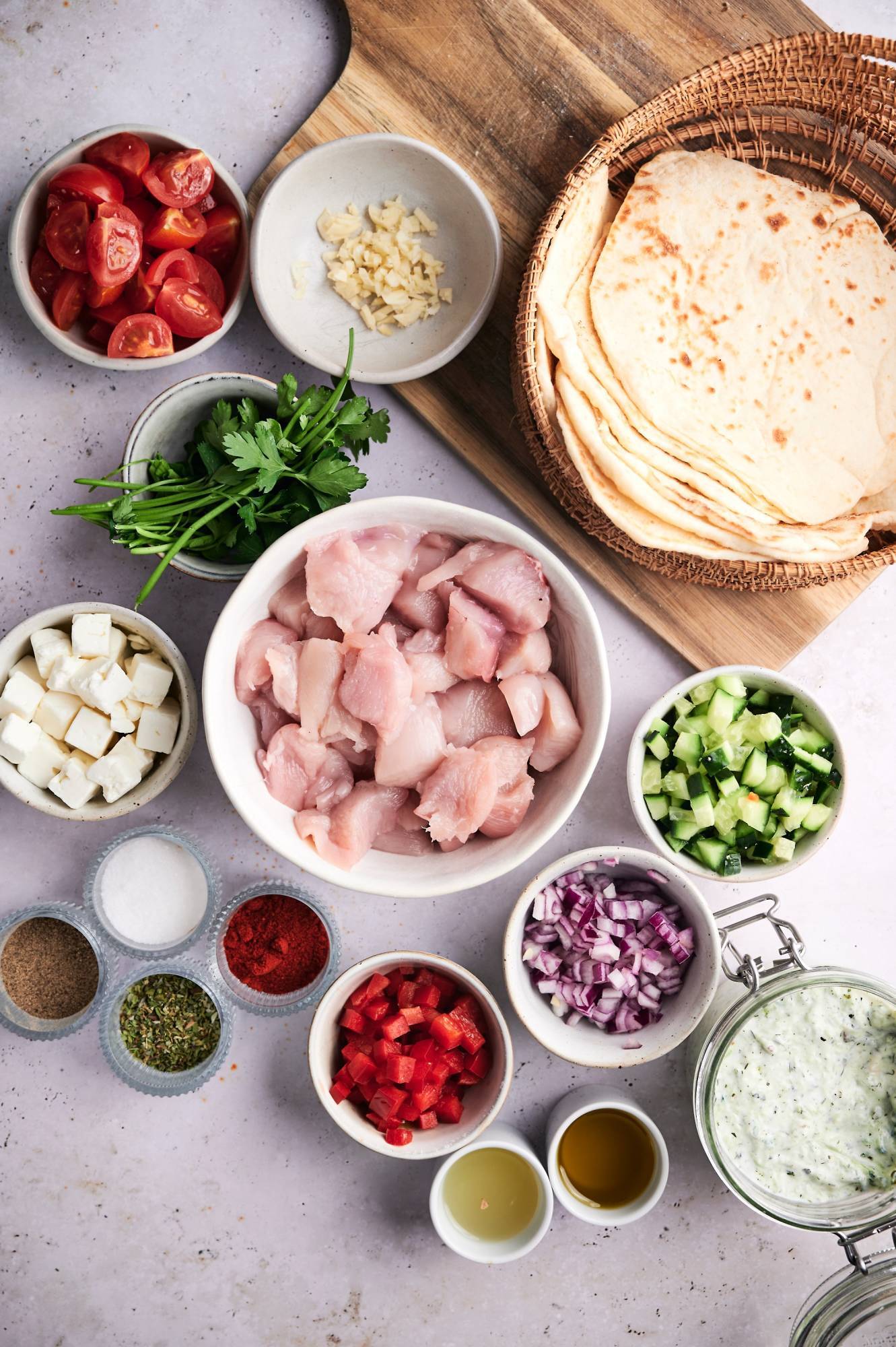 Ingredients for Mediterranean Chicken Tacos including chicken breast, garlic, oregano, tomatoes, red onion, feta cheese, olives, pita bread, and spices.