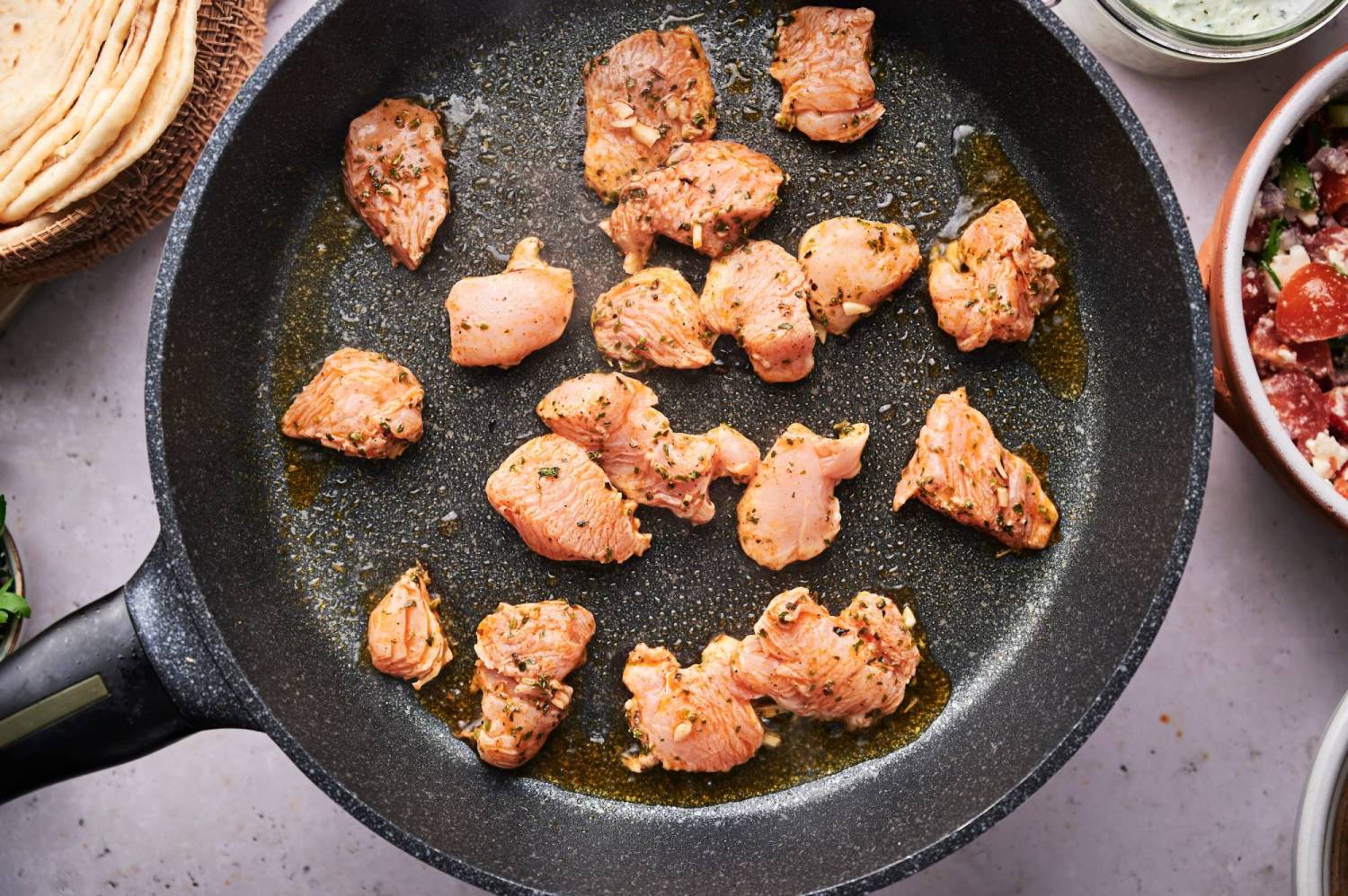 Mediterranean chicken pieces cooking in a skillet with browned edges.