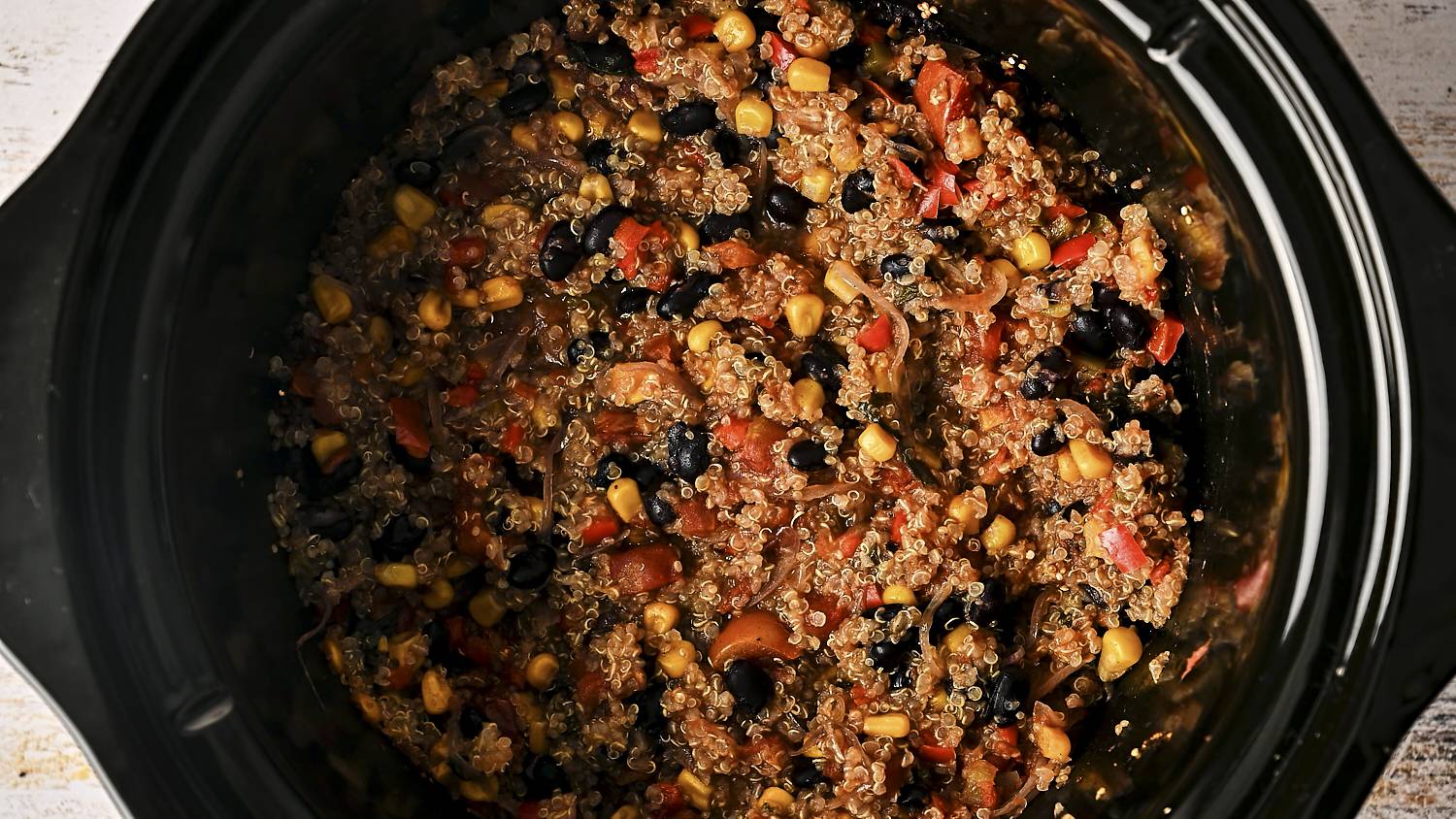 Cooked Mexican quinoa with black beans, corn, tomatoes, and spices in a slow cooker, ready to serve.