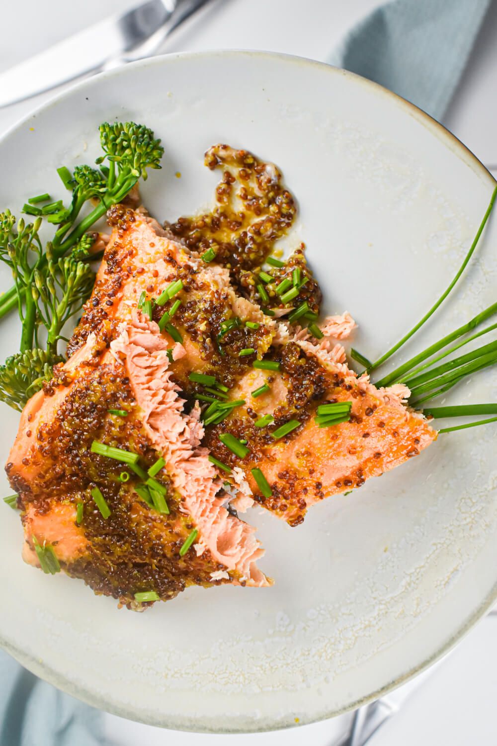 Mustard maple salmon cooked and sliced in half on a plate with sauce and broccoli.