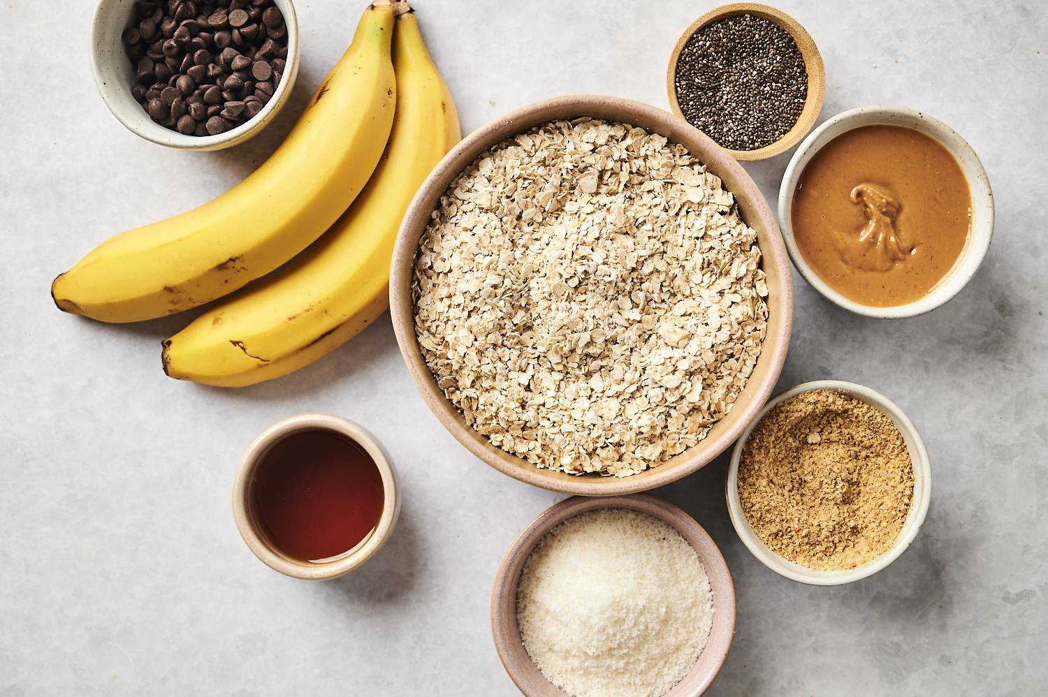 Ingredients for no bake oatmeal bars including rolled oats, peanut butter, chia seeds, coconut, flaxseed meal, maple syrup, and chocolate chips.