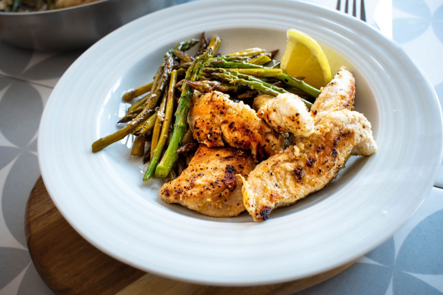 Crispy lemon garlic chicken and sautéed asparagus wit fresh lemon in a white bowl.