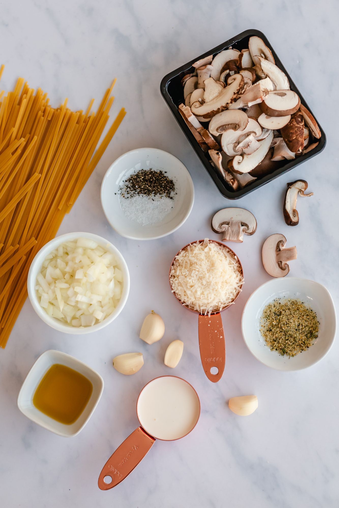 Ingredients to make creamy mushroom pasta including sliced mushroom, garlic, onion, cream, spaghetti, and Parmesan cheese.