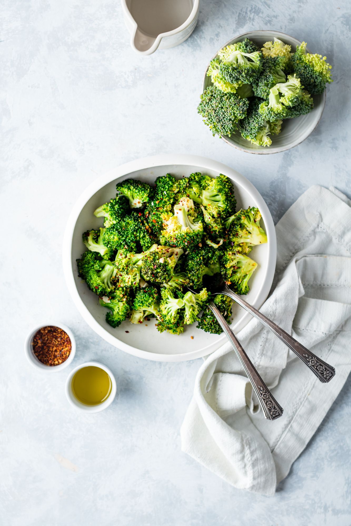 Broccoli that has been pan fried with garlic in a white bowl with olive oil on the side.