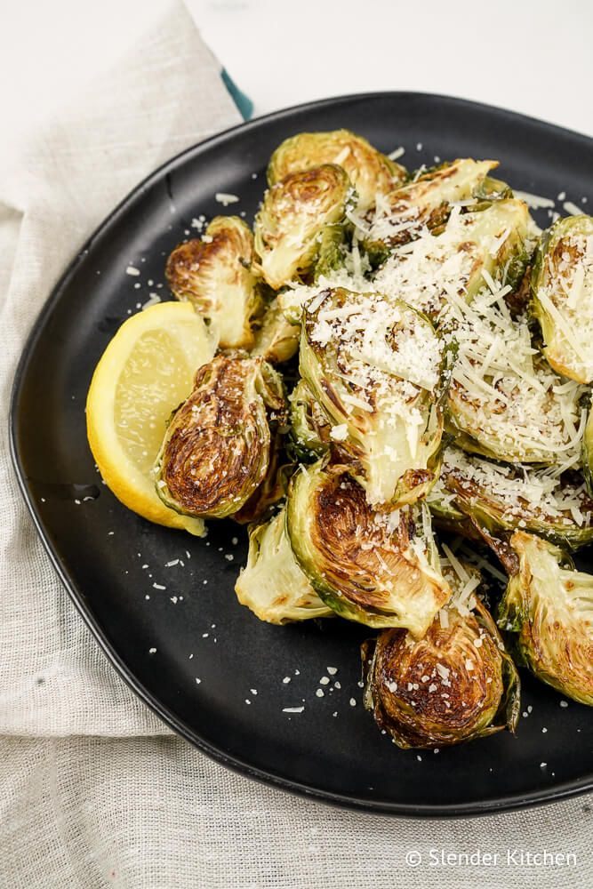 Parmesan Brussels Sprouts with lemon on a black plate.
