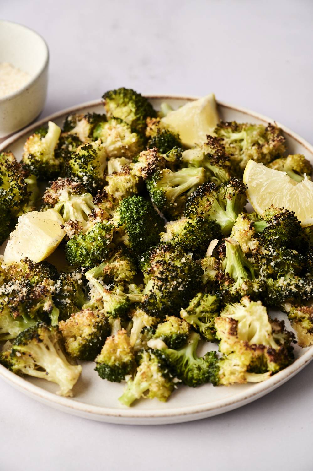 Oven-roasted broccoli florets with a crispy texture, topped with seasoning, served on a plate with lemon wedges for garnish.