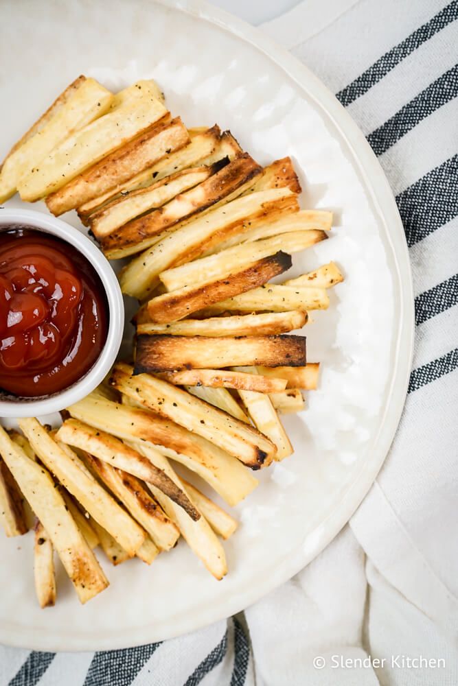 Roasted parsnip fries on a plate with a side of ketchup.