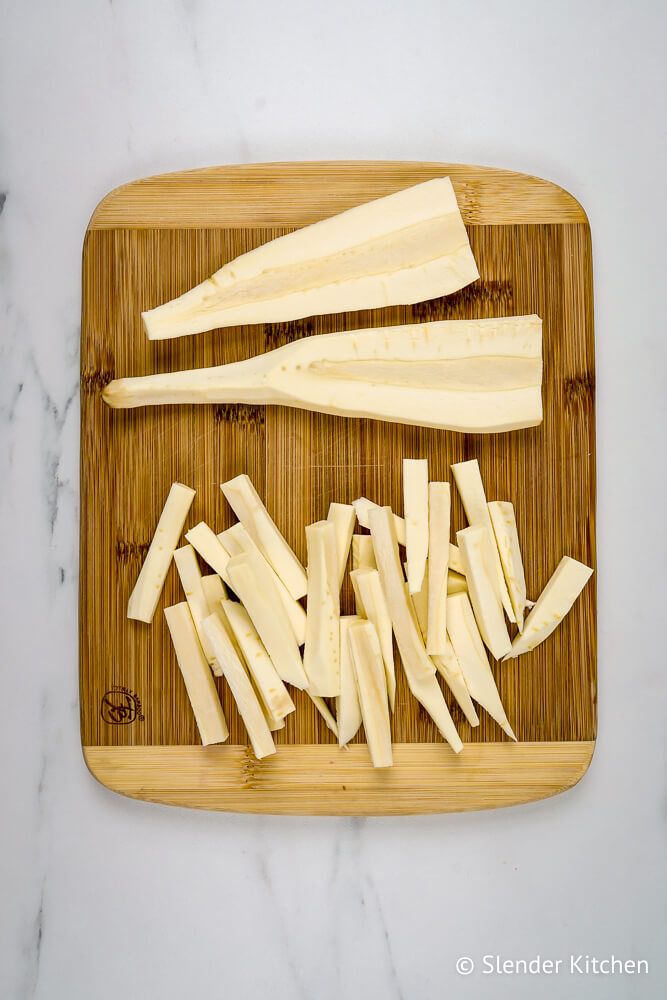 Parsnips that are peeled and cut into match stick fries on a cutting board.