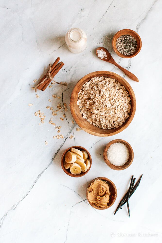 Ingredients for overnight oatmeal with peanut butter, banana, vanilla, chia seeds, and more on a marble board.