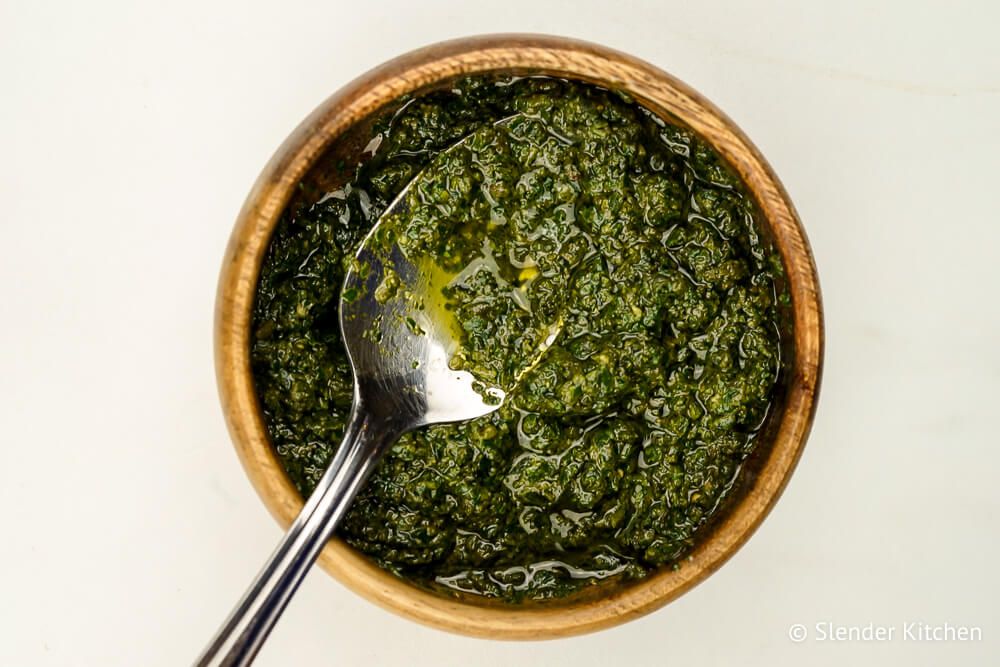 Homemade pesto in a wooden bowl with a spoon.