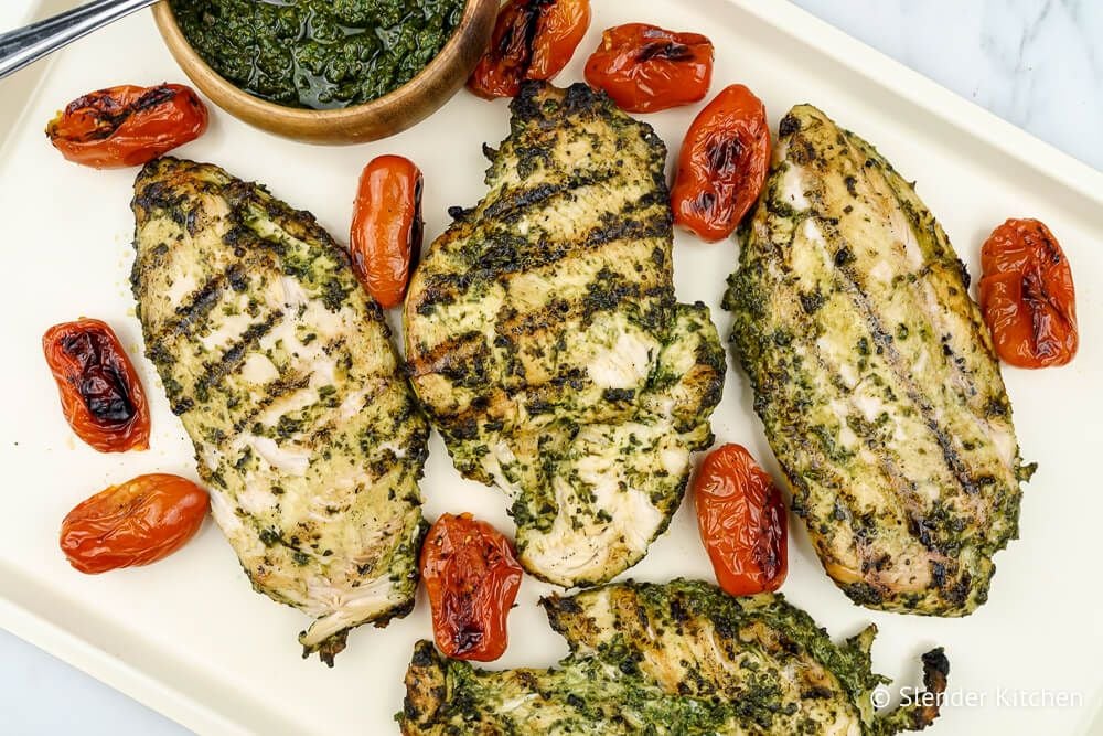 Healthy Pesto grilled chicken on a baking sheet next to a bowl of homemade pesto.