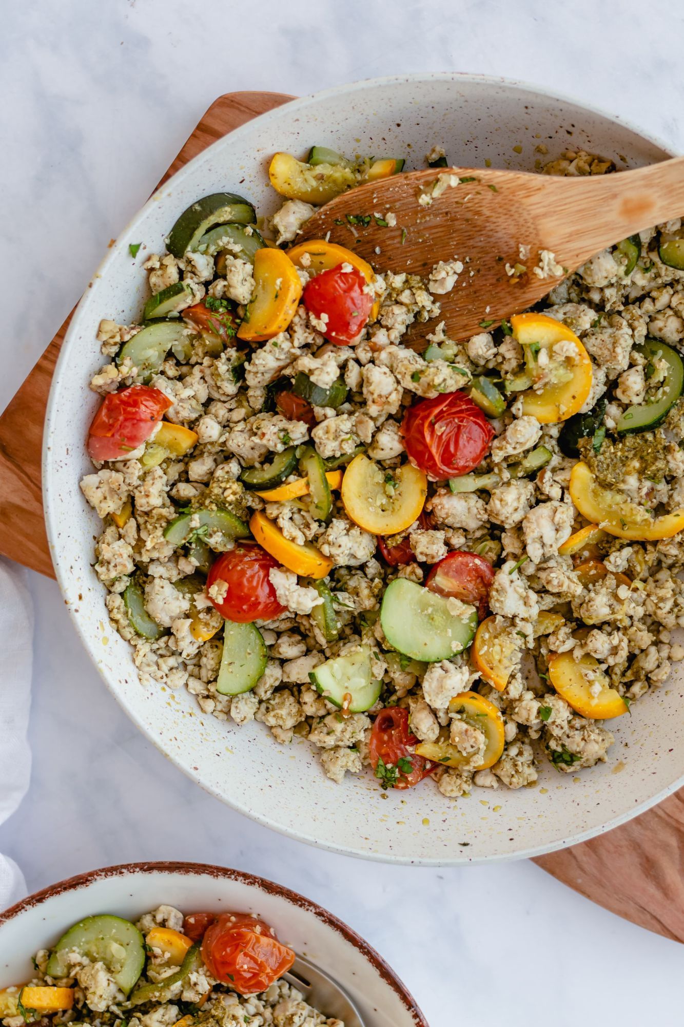 Ground turkey cooked with pesto, zucchini, and tomatoes served in a plate with fresh parsley.