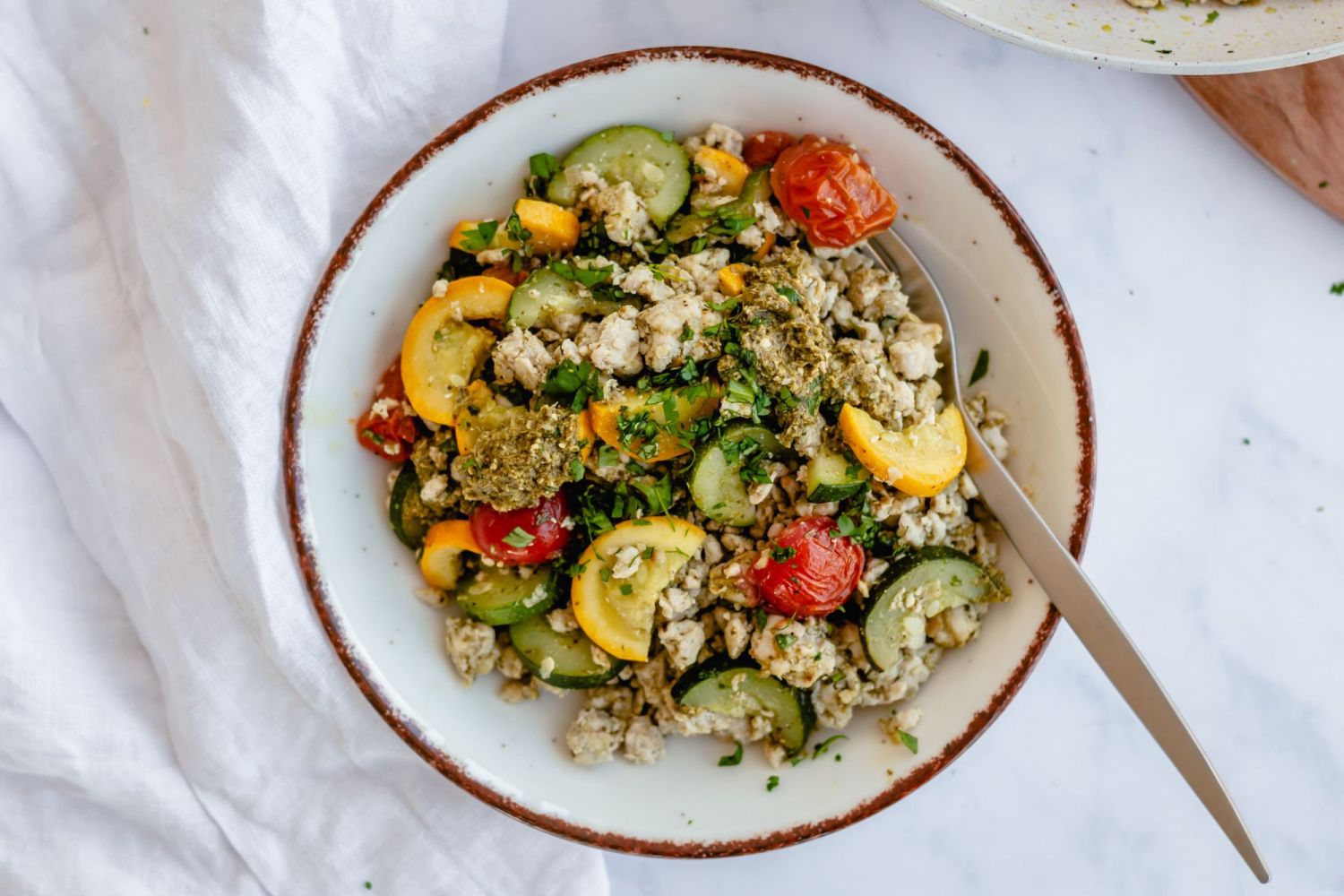 Bowl filled with pesto ground turkey, cherry tomatoes, onion, zucchini, and summer squash.