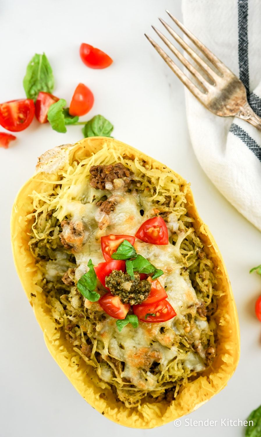 Low carb Pesto Spaghetti Squash on a marble background with tomato slices.
