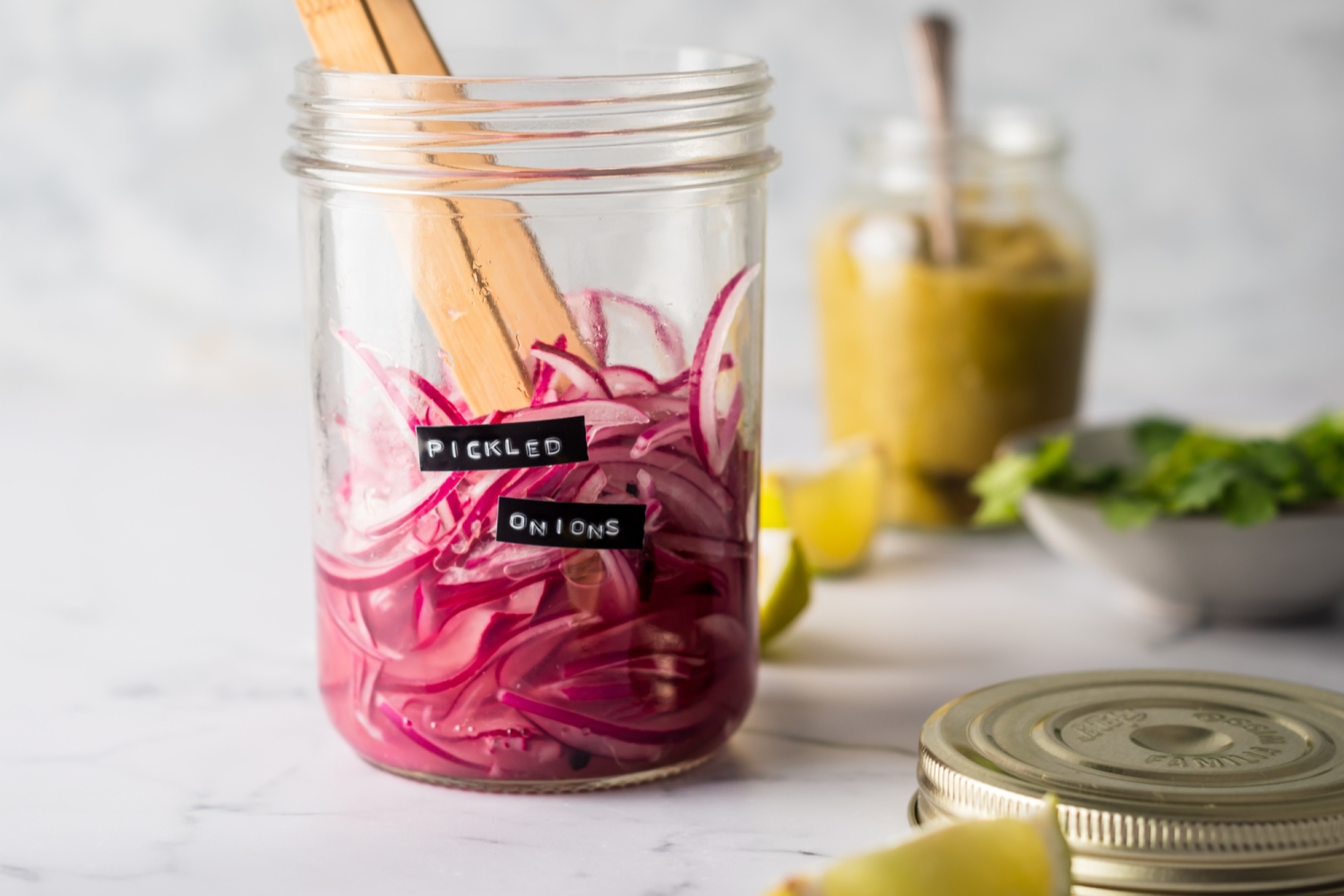 Jar with pickled red onions and lime juice with wooden tongs.