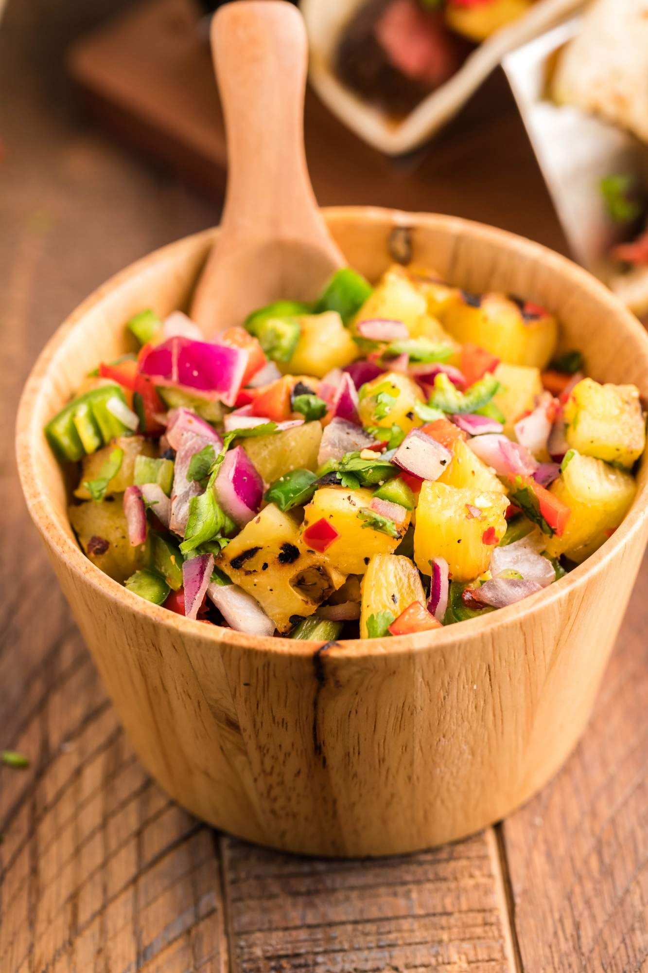 Pineapple serrano salsa with cilantro, red onion, lime juice, and grilled pineapple in a wooden bowl.