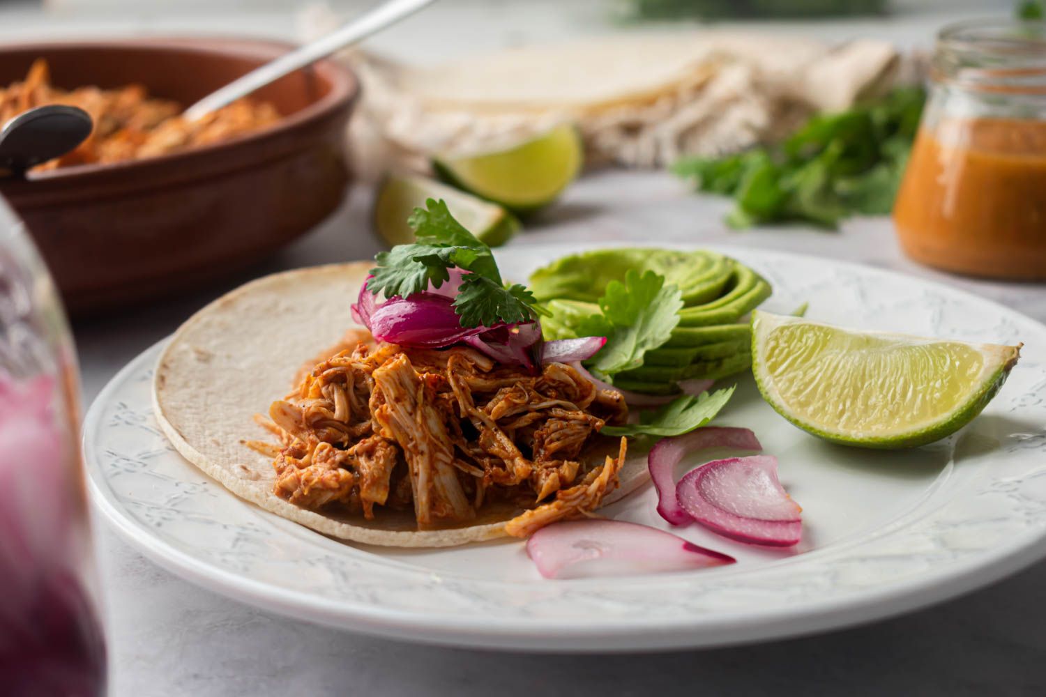 Taco with pollo pbili, pickled red onioins, cilantro, and habanero salsa in a corn tortilla on a plate with limes.
