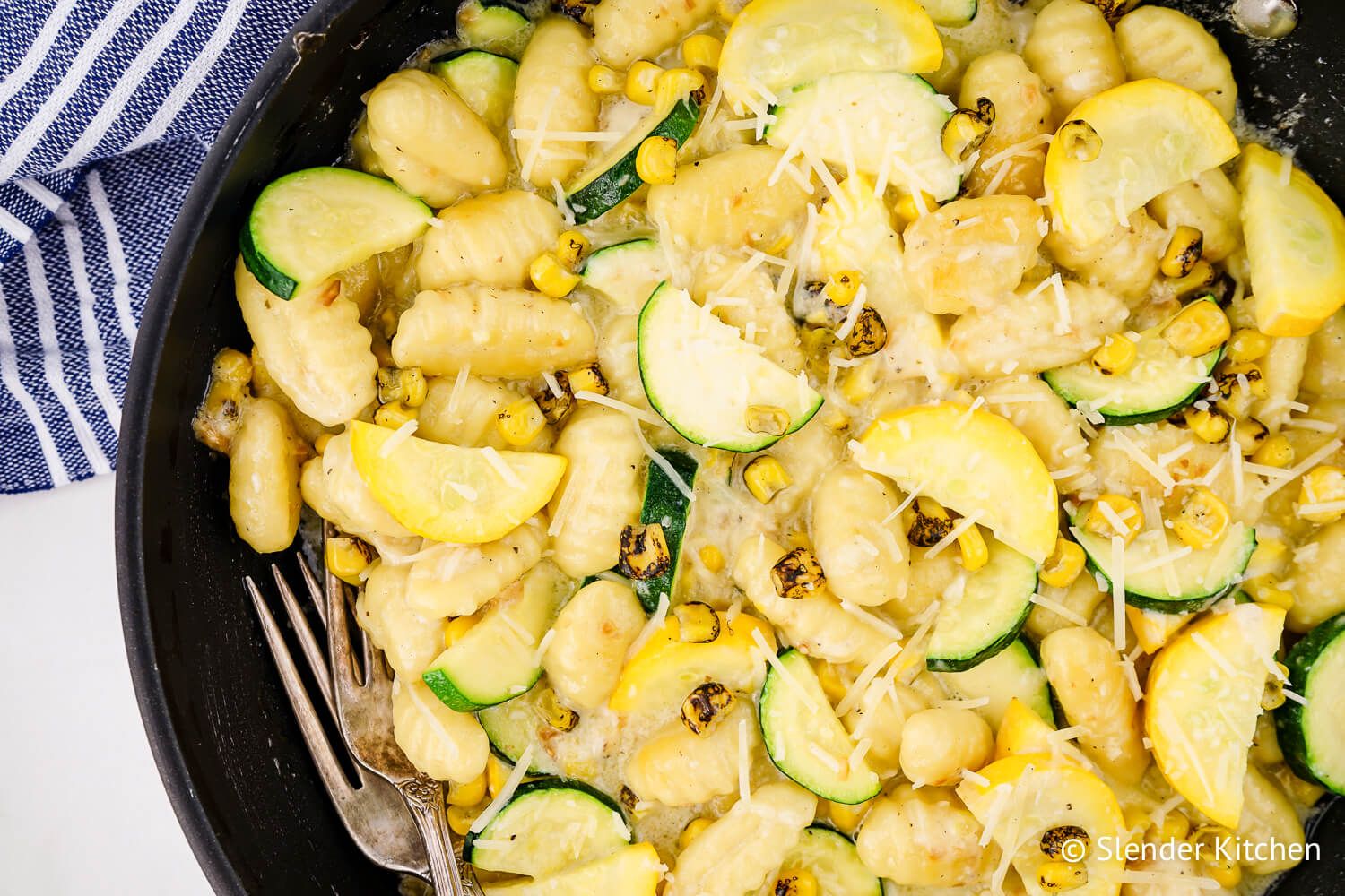 Potato gnocchi recipe in a skillet with zucchini, summer squash, and corn with a blue napkin.