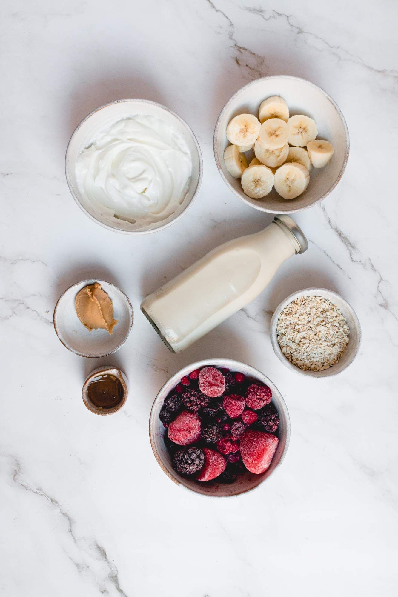 Ingredients for a banana berry smoothie including frozen berries, bananas, yogurt, oats, peanut butter, and honey.