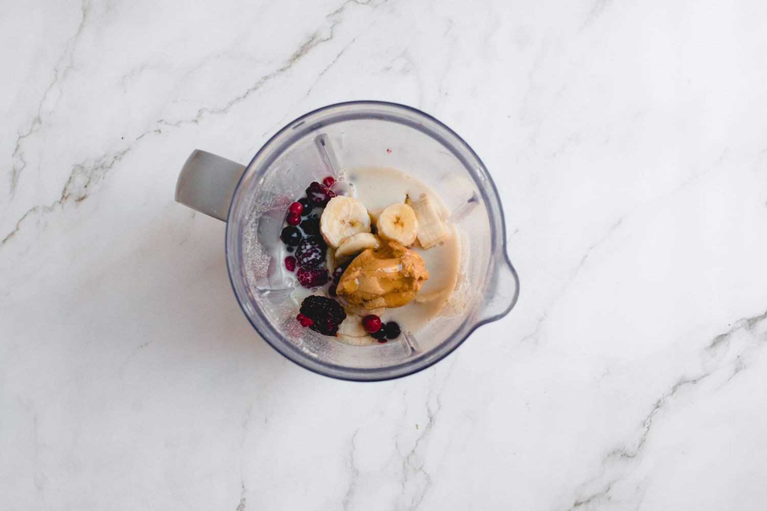 Blender with peanut butter, bananas, frozen berries, oats, yogurt, and almond milk.
