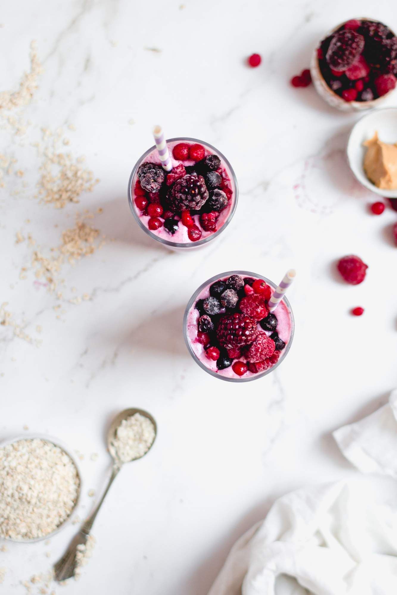 Berry banana smoothie in two glasses with frozen berries on top and loose oats on the size.