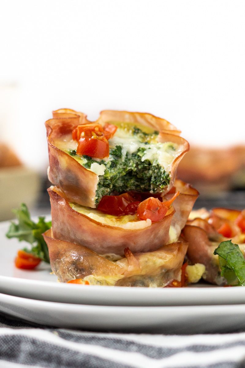 Spinach and ham quiche cupcakes with mozzarella cheese piled in a stack with cherry tomatoes on top.